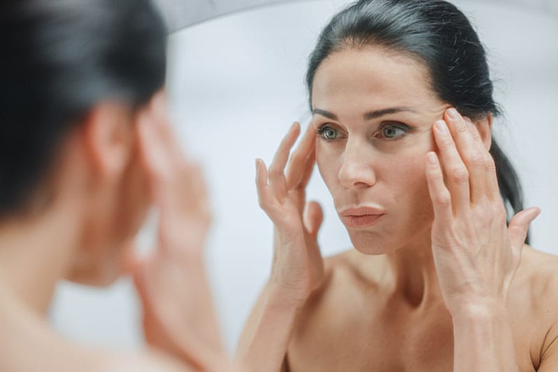 woman looking in the mirror after her mini facelift in Boston, MA